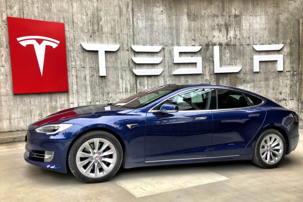 a blue Tesla car parked in front of a Tesla sign.
